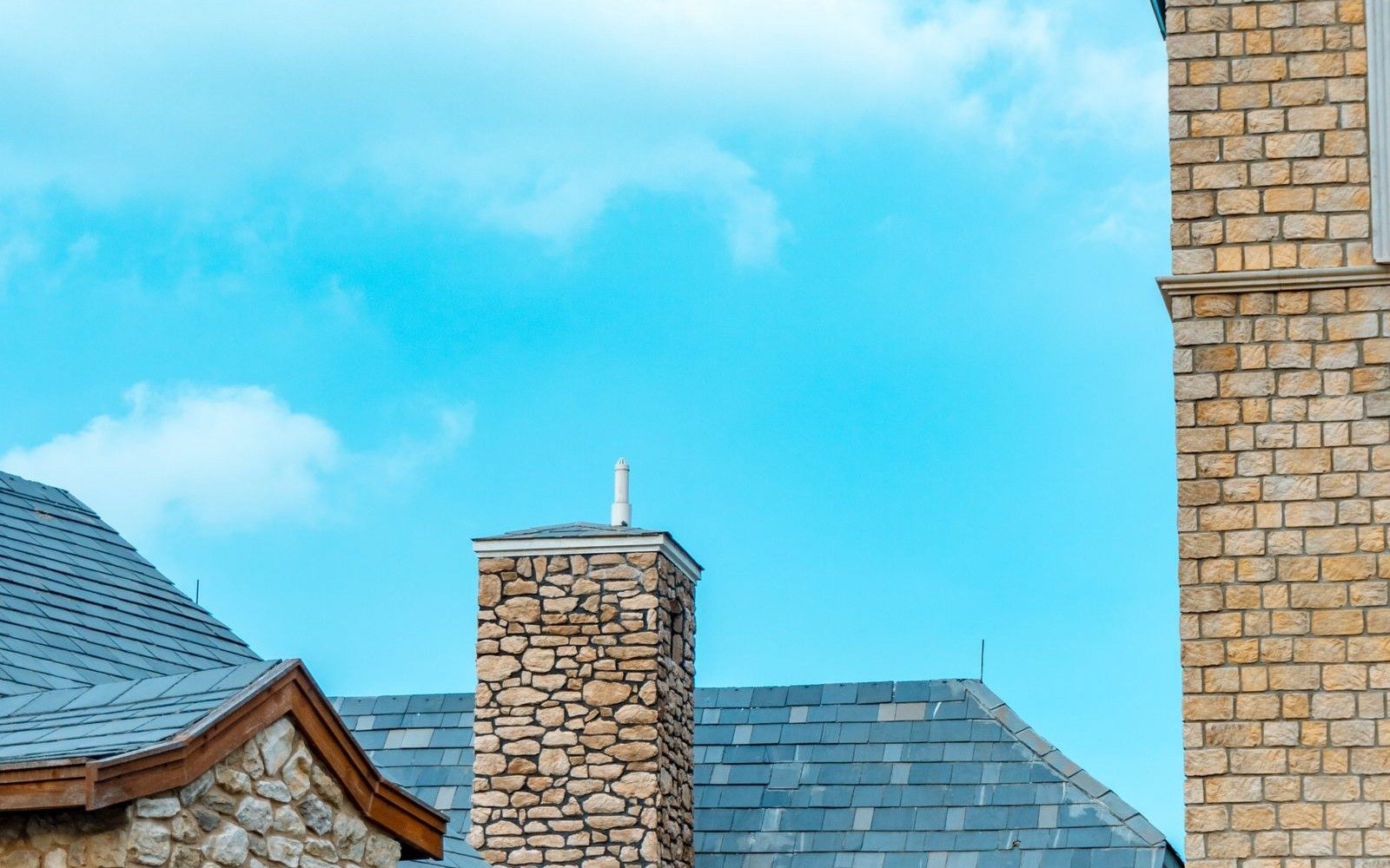 Slate roofs and a stone chimney against a blue sky